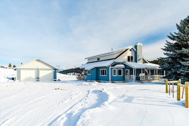 snow covered property featuring covered porch, an outbuilding, a garage, and a chimney
