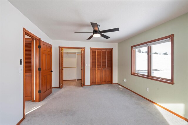 unfurnished bedroom featuring light colored carpet, multiple closets, baseboards, and a ceiling fan