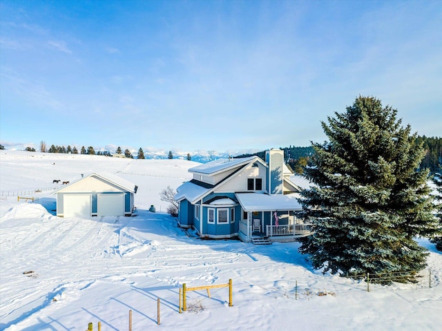 snow covered back of property with a chimney, covered porch, and an outdoor structure