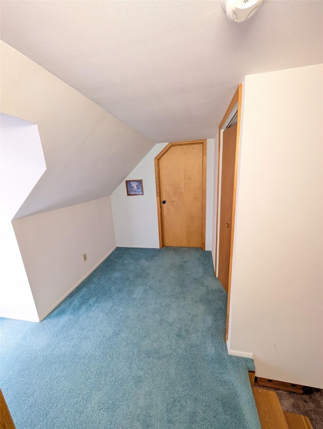 additional living space featuring vaulted ceiling, dark carpet, and a textured ceiling