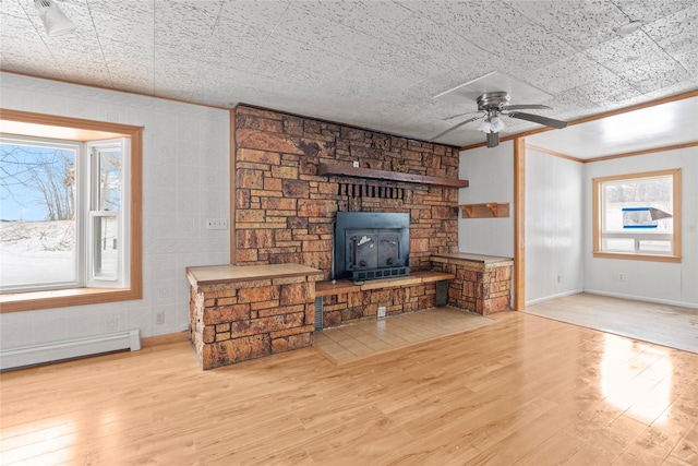 living room featuring a baseboard heating unit, a stone fireplace, light wood-style flooring, and crown molding