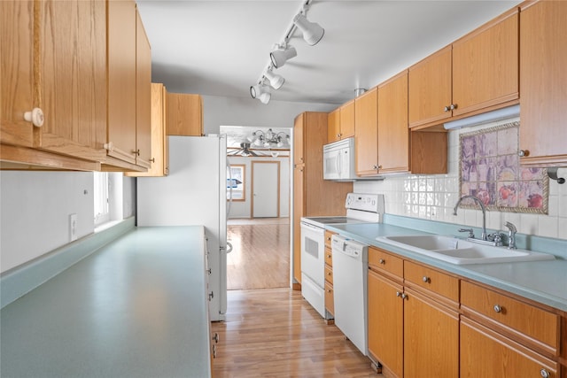 kitchen with light countertops, light wood-style flooring, decorative backsplash, a sink, and white appliances