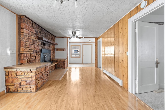 unfurnished living room featuring a wood stove, ceiling fan, wooden walls, and light wood finished floors