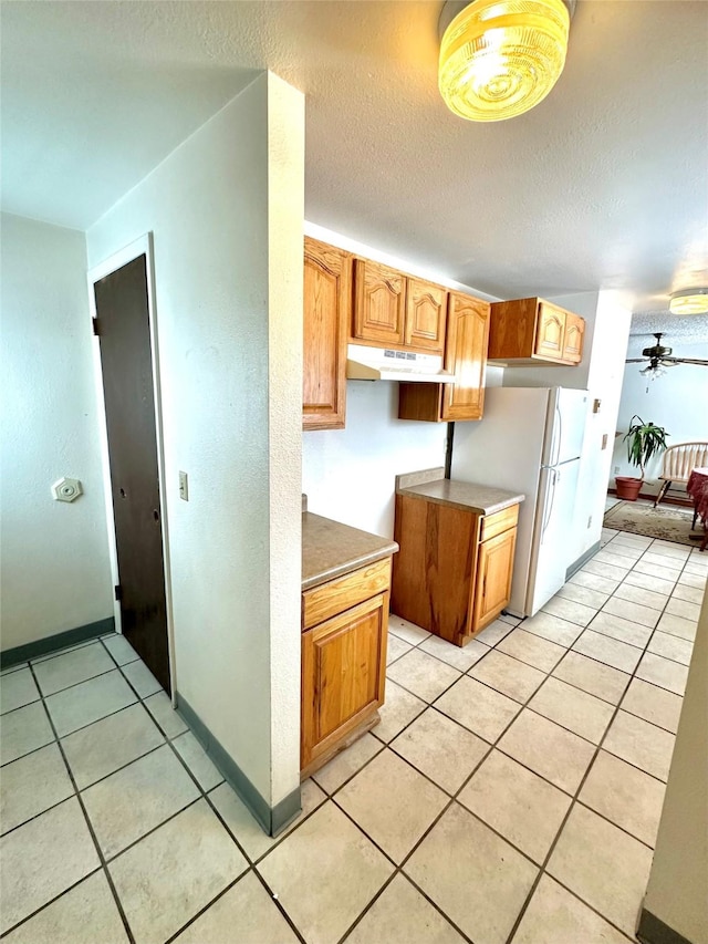 605 Idaho St, Deer Lodge, MT 59722 - kitchen with under cabinet range hood, light tile patterned flooring, a textured ceiling, a ceiling fan, and freestanding refrigerator