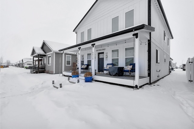 snow covered back of property featuring covered porch