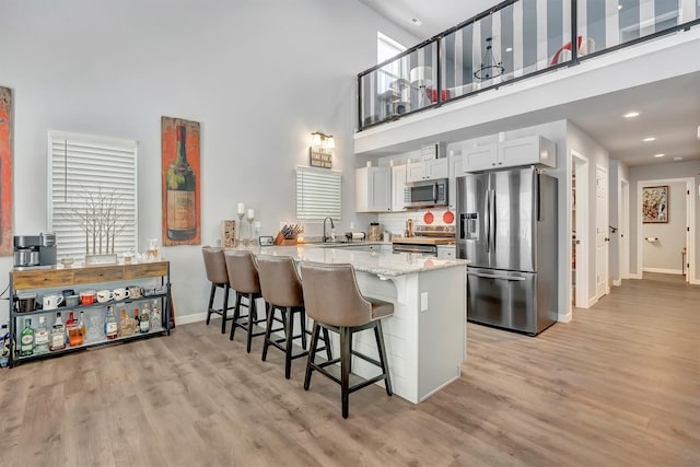 kitchen with a breakfast bar, a towering ceiling, stainless steel appliances, white cabinets, and kitchen peninsula