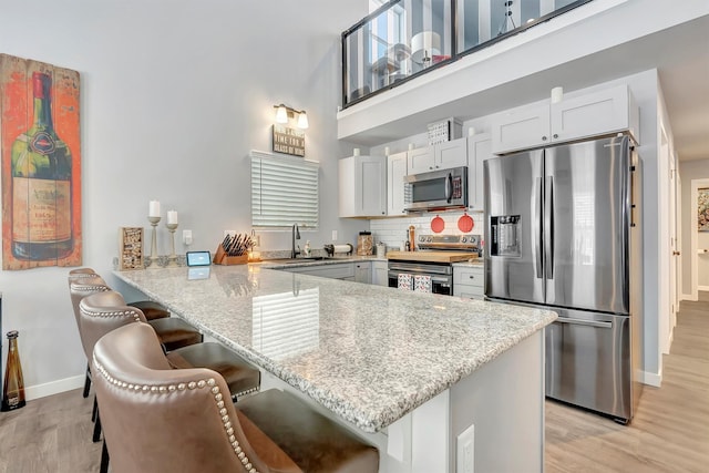 kitchen with appliances with stainless steel finishes, sink, a breakfast bar area, white cabinets, and kitchen peninsula