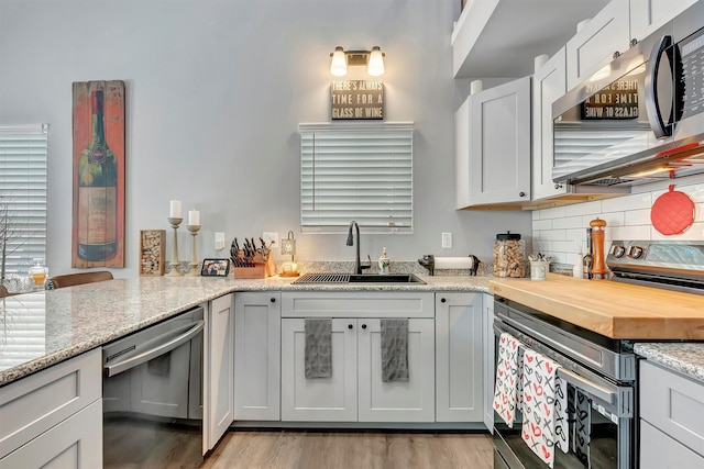 kitchen featuring sink, appliances with stainless steel finishes, backsplash, light stone countertops, and white cabinets