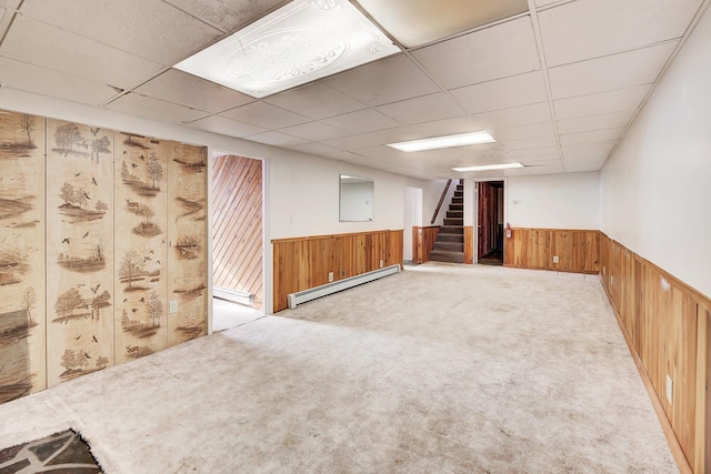 carpeted spare room featuring a baseboard heating unit, a paneled ceiling, and wood walls