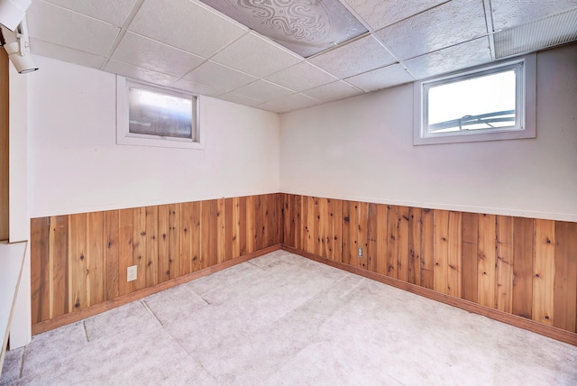 basement with a paneled ceiling, light colored carpet, and wood walls