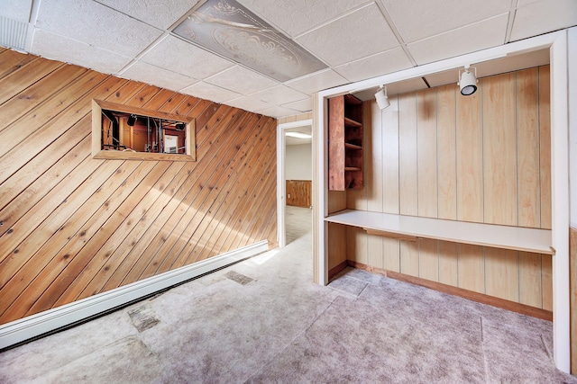 basement featuring light carpet, a drop ceiling, and wooden walls