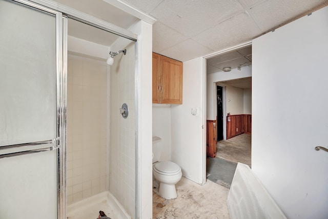 bathroom with a paneled ceiling, a shower with door, concrete floors, and toilet