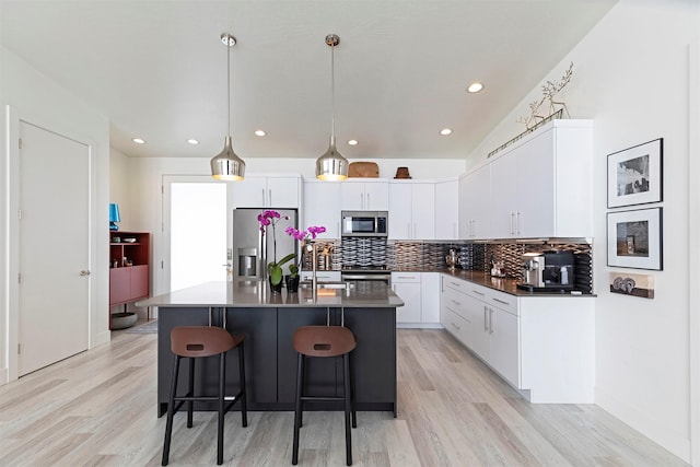 kitchen featuring a breakfast bar, dark countertops, decorative backsplash, appliances with stainless steel finishes, and white cabinetry