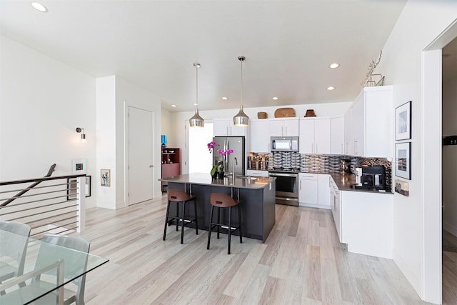 kitchen with appliances with stainless steel finishes, white cabinetry, decorative light fixtures, an island with sink, and a breakfast bar area