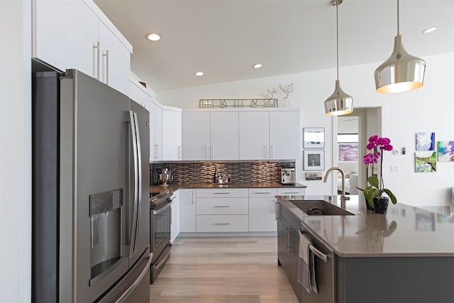 kitchen featuring lofted ceiling, a sink, appliances with stainless steel finishes, tasteful backsplash, and dark countertops