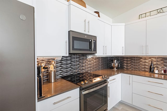 kitchen with lofted ceiling, white cabinetry, stainless steel appliances, and decorative backsplash