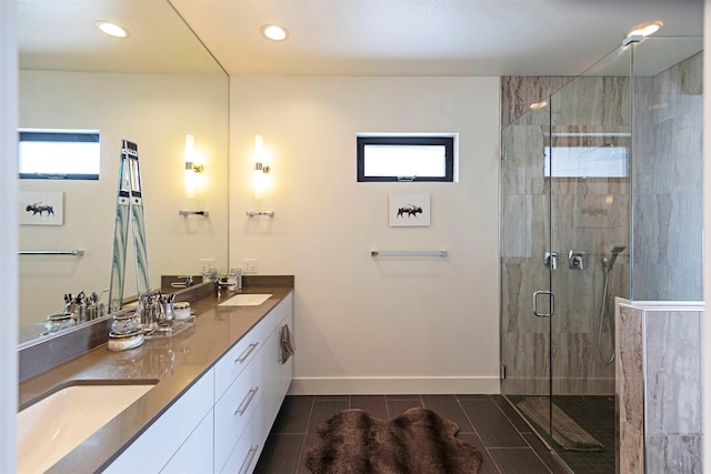 bathroom with double vanity, a shower stall, baseboards, and a sink