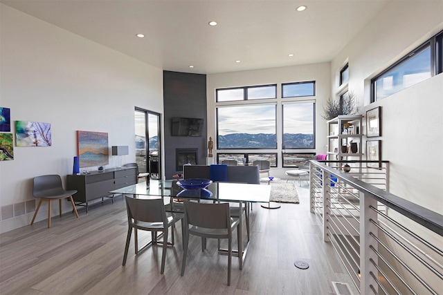 dining area featuring recessed lighting, visible vents, a towering ceiling, a large fireplace, and wood finished floors