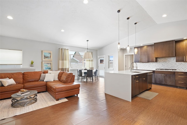 kitchen featuring a center island with sink, lofted ceiling, sink, wall chimney range hood, and dark brown cabinetry