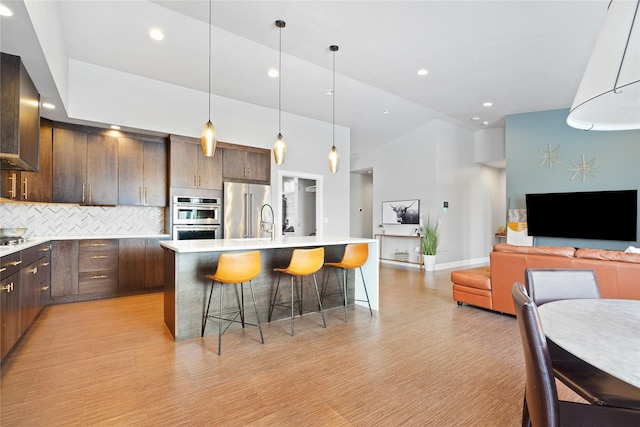 kitchen with a kitchen island with sink, dark brown cabinets, tasteful backsplash, appliances with stainless steel finishes, and a breakfast bar area