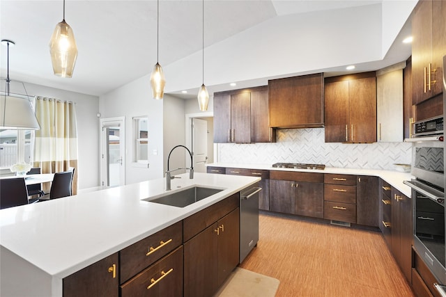 kitchen with a center island with sink, stainless steel appliances, decorative light fixtures, vaulted ceiling, and sink