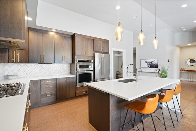 kitchen with sink, stainless steel appliances, dark brown cabinets, a breakfast bar area, and a kitchen island with sink