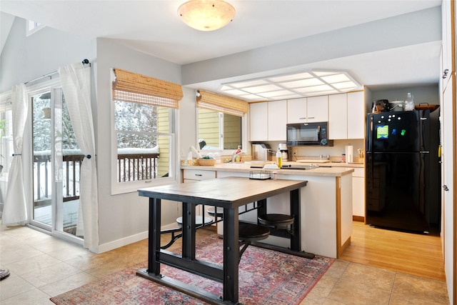 kitchen featuring light tile patterned floors, light countertops, white cabinets, black appliances, and baseboards