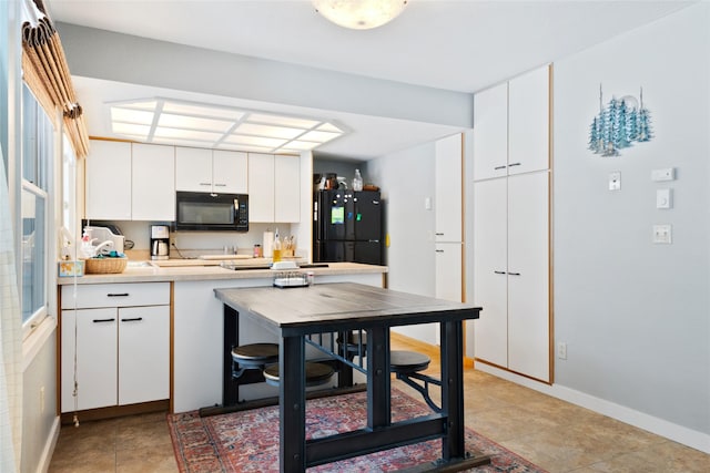 kitchen with baseboards, light countertops, black appliances, white cabinetry, and light tile patterned flooring