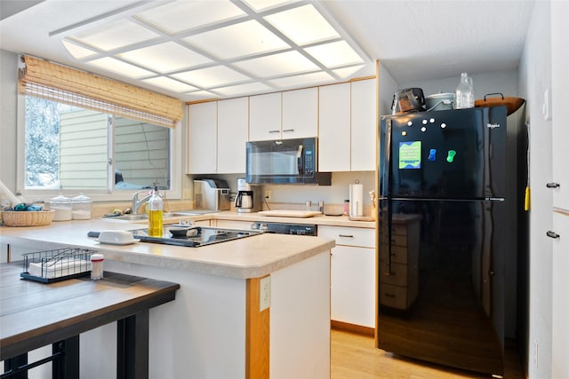 kitchen featuring light countertops, light wood-style floors, white cabinets, a sink, and black appliances