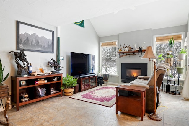 living area featuring vaulted ceiling, light tile patterned floors, a glass covered fireplace, and a wealth of natural light