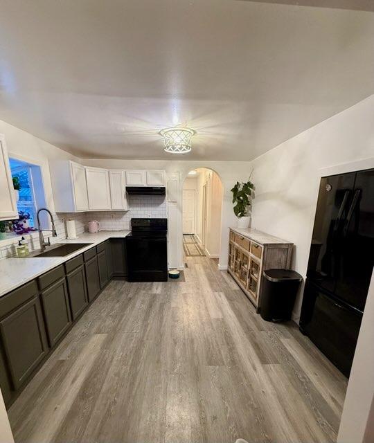 kitchen with light hardwood / wood-style flooring, sink, black electric range, white cabinets, and decorative backsplash