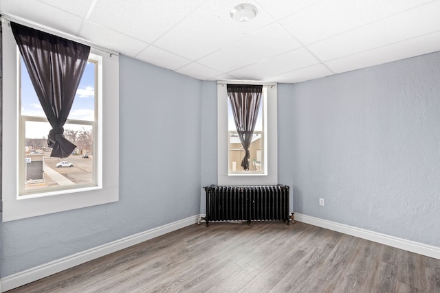 unfurnished room with a paneled ceiling, radiator, and wood-type flooring