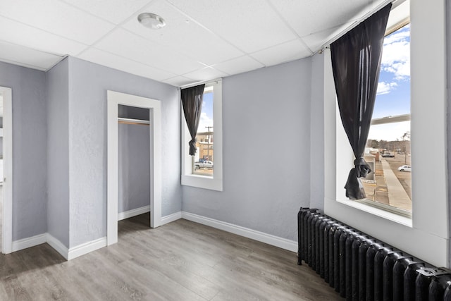 bedroom with hardwood / wood-style floors, multiple windows, a paneled ceiling, and radiator