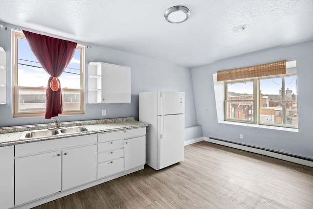 kitchen featuring white fridge, sink, a baseboard heating unit, and white cabinets