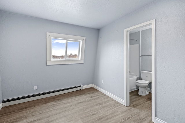 unfurnished bedroom featuring a textured ceiling, connected bathroom, light hardwood / wood-style floors, and baseboard heating