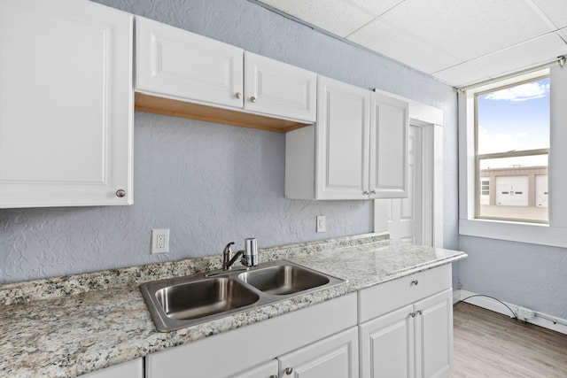 kitchen with sink, white cabinets, light stone countertops, and light hardwood / wood-style floors