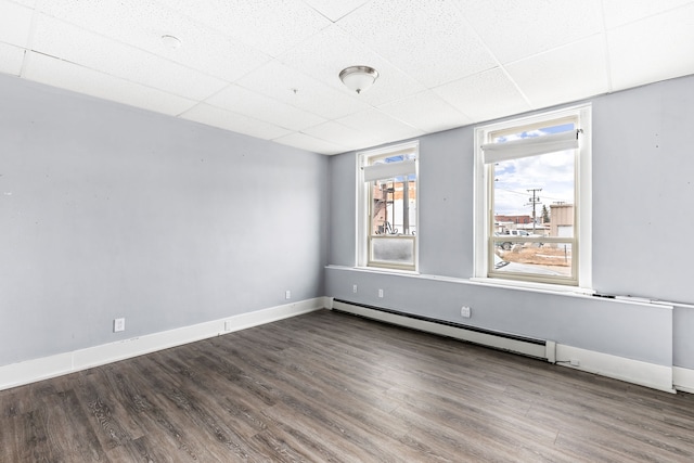 empty room featuring baseboard heating, a paneled ceiling, and dark hardwood / wood-style floors