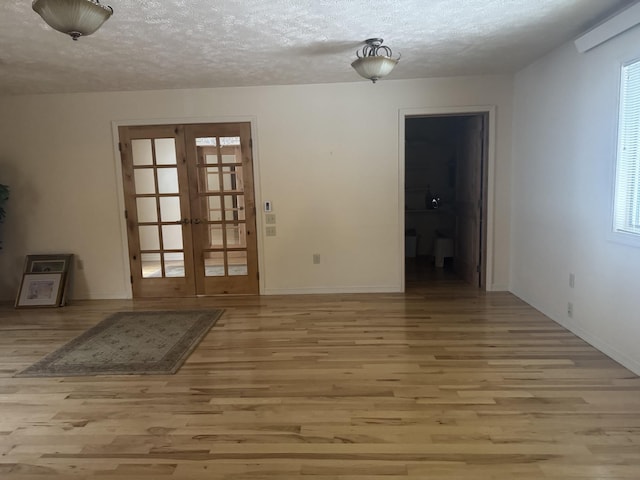 empty room featuring a textured ceiling, french doors, and light hardwood / wood-style floors