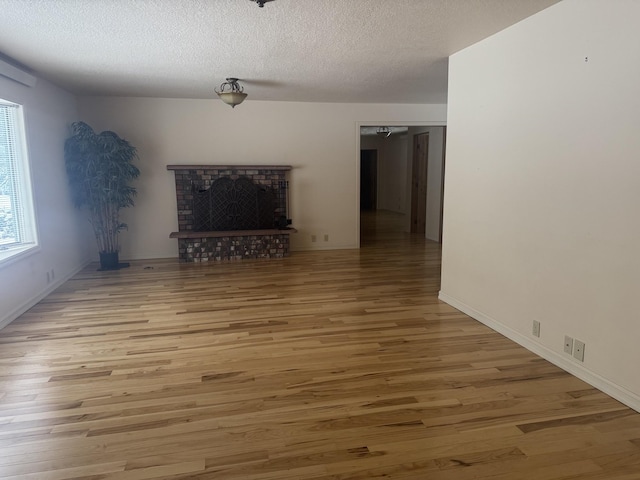 unfurnished living room with light wood-type flooring, a brick fireplace, and a textured ceiling