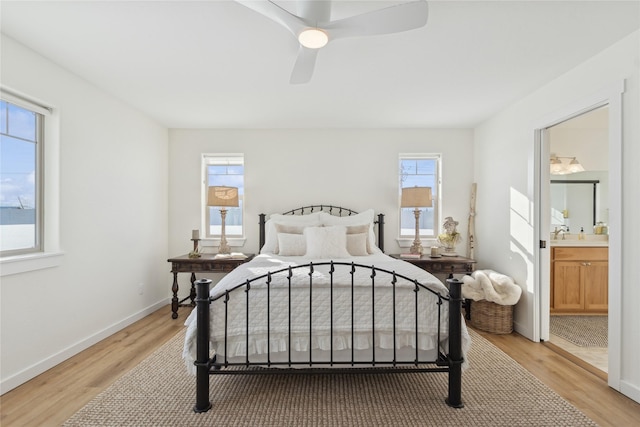 bedroom with light wood-style floors, ensuite bath, baseboards, and a ceiling fan