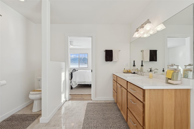 ensuite bathroom with toilet, connected bathroom, vanity, and baseboards