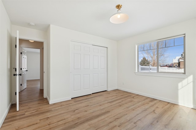 unfurnished bedroom featuring light wood finished floors, baseboards, and a closet