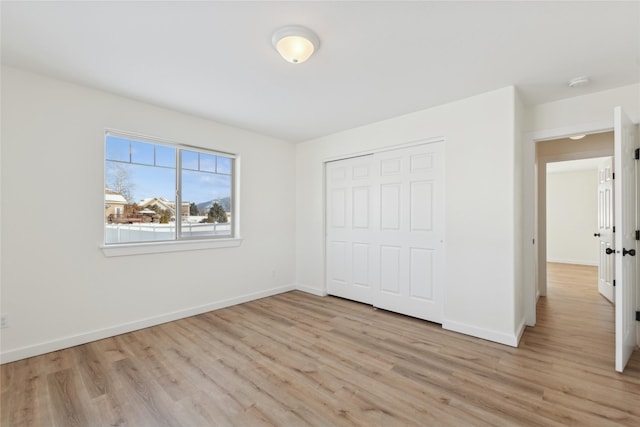 unfurnished bedroom featuring light wood-style floors, a closet, and baseboards