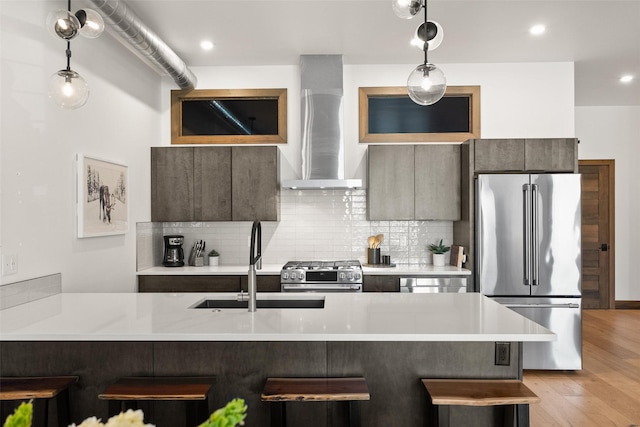 kitchen featuring sink, backsplash, stainless steel appliances, wall chimney exhaust hood, and a kitchen breakfast bar