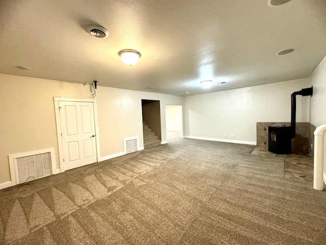 finished basement with a wood stove, stairway, visible vents, and dark colored carpet