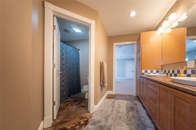 full bath featuring double vanity, toilet, backsplash, and a sink