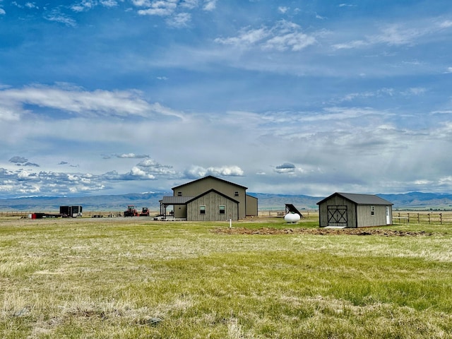 view of yard featuring an outbuilding, a rural view, a storage unit, fence, and a mountain view