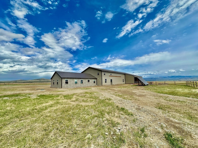 back of house with a rural view, fence, and a lawn