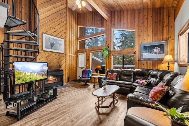 living room with wooden walls, high vaulted ceiling, wooden ceiling, a lit fireplace, and stairs