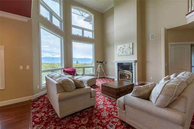 living room with dark wood finished floors, visible vents, ornamental molding, a glass covered fireplace, and baseboards